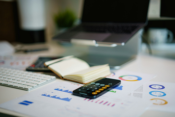 Desk with a laptop, calculator, notebook and papers with diagrams.