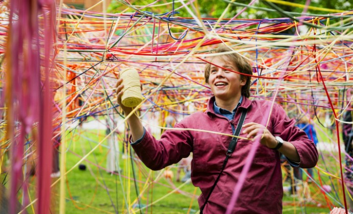 Student in a colorful web of yarns in a park in Lund. Skissernas museum